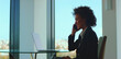 © Videophilia - Confident businesswoman smiling while having a phone conversation, using a mobile device in a contemporary high-rise office with a laptop on a glass table