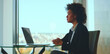 © Videophilia - Thoughtful black businesswoman working on laptop, sitting at a modern glass desk in a bright corporate office with a large window, contemplating new business strategies while looking away