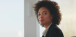 © Videophilia - Confident black businesswoman glancing at camera, wearing a formal suit in an office setting, representing professionalism, success, leadership, and diverse workforce concepts