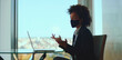© Videophilia - Black businesswoman in a modern office wearing a protective face mask while conducting a laptop video conference, gesturing during a virtual meeting with city view daylight