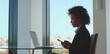 © Videophilia - Businesswoman focused on smartphone while analyzing financial charts on a laptop at a glass desk with city view, representing digital trading, investment and market analysis