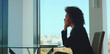 © Videophilia - African american businesswoman sitting at a glass table in a modern office, thoughtfully looking out the window at the city skyline while considering professional challenges and career prospects
