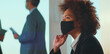 © Videophilia - Young black businesswoman wearing a protective face mask while focusing on a presentation during a corporate meeting, adapting to new normal and health precautions