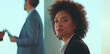© Videophilia - Young professional african american businesswoman with an afro hairstyle looking directly at the camera with a confident smile during a corporate meeting or event in a modern office environment