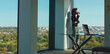 © Videophilia - Businesswoman standing by an office window, enjoying a coffee break while observing the expansive city view, a laptop positioned on a modern glass desk nearby, reflecting a moment of contemplation