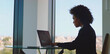 © Videophilia - Professional businesswoman using a laptop to analyze financial data, working focused in a modern office with a city view through large windows, symbolizing corporate success