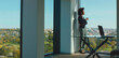 © Videophilia - Professional businesswoman standing by the large office window, holding a coffee cup, taking a thoughtful break from work, enjoying a panoramic city and park view on a bright day