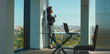 © Videophilia - Young businesswoman with curly hair standing by a large office window, holding a coffee cup, looking out at the sprawling city skyline below while taking a thoughtful break from work