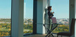 © Videophilia - Confident businesswoman with curly hair standing by large office window, enjoying a warm beverage and looking at the urban landscape, reflecting on career success and future aspirations