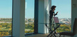 © Videophilia - Black businesswoman wearing a face mask standing in a modern office space, talking on a mobile phone with a cityscape and green park visible through large windows