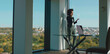 © Videophilia - Young african american businesswoman on a phone call in a modern high-rise office, standing by the window with laptop on glass table, looking out over the cityscape, confident and focused