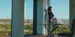 © Videophilia - Businesswoman on phone by a large office window, gazing at a green city skyline and park, embodying confident professional communication, leadership and urban workplace vision