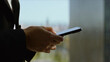 © Videophilia - Professional businessperson hands holding a smartphone, interacting with technology and communicating during work hours, standing near a window with a blurred background