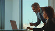 © Videophilia - Experienced mentor guiding young trainee, collaborating on a project using a laptop in a modern office with a city view, fostering teamwork and professional development