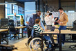 © .shock - Diverse business team collaborating in a modern office environment. A woman in a wheelchair works on a laptop while colleagues explore virtual reality and digital tools, promoting innovation
