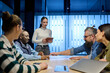 © .shock - Diverse business team gathered around a table discussing analytics during a meeting in a modern office. Laptop screen shows charts and graphs, symbolizing teamwork, communication, and data driven
