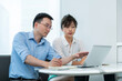 © xy - Two asian businesspeople working together in the office while using laptop
