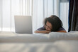 © shine - Tired asian middle aged woman sleeping on bed in front of laptop, Comfortable bed with soft blanket, inviting bedroom scene in morning sunlight.