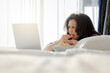 © shine - Elegant middle-aged asian woman eating popcorn and watching movie on laptop while resting on bed. Sun shines from the apartment window in bedroom. Copy space
