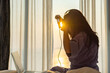 © shine - Beautiful Asian businesswoman using Curling iron or Hair straightener and working with her laptop while sitting on bed getting ready for work in the morning with warm sunlight.