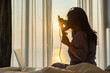 © shine - Asian middle aged woman taking care of her hair and curling hair with electric iron curler tong, getting ready for travel on vacation. Sunshines on her from the big window. Happy woman greets new day.