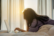 © shine - Fatigued mature businesswoman working on laptop, resting her chin on her hand, thinking while lying on bed in bright sunlight from the window. Calmness and Warm sun.