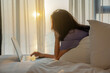 © shine - Beautiful middle aged asian woman typing e-mail contact client on laptop, search data online, focus on screen after waking up on bed. A room with comfortable, warm sunlight coming through the window.
