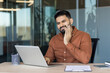 © Liubomir - Young man experiencing dental pain while working on his laptop in a modern office, stopping work due to the discomfort and needing to visit a dentist for relief