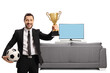 © Ljupco Smokovski - Man in a suit holding a trophy cup and football in front of tv and sofa