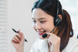 © PRIME STOCK LAB - Young woman customer service representative smiling while speaking with headset and holding pen