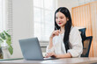 © PRIME STOCK LAB - Young woman working on laptop in bright home office, thoughtful expression, modern desk plant, natural light, remote work vibe