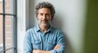 © vadosloginov - Middle-aged man with curly hair stands confidently against a bright wall during daylight in a cozy indoor setting