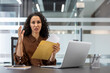 © Liubomir - Young professional woman feeling upset and confused after opening a critical document from a brown envelope at her desk. Processing unexpected information during a difficult moment in her business day