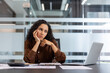 © Liubomir - Businesswoman experiencing burnout and feeling pensive while working on a laptop at her modern office desk, reflecting on her workload and professional challenges