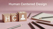 © DesignIDN - This stock photo illustrates the concept of human centered design with wooden blocks, notepad, and pencils on a pink surface, symbolizing innovation.