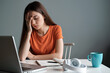 © chris3d - A young woman wearing an orange shirt looks overwhelmed while studying at a desk in her home. Generative AI.