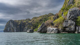 Picturesque coastal cliffs and boulders. Green tropical vegetation on the slope. A calm turquoise ocean. Blue sky, clouds. Philippines. Palawan.