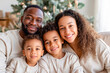 © Irina - A smiling family of four cuddles on a couch with a decorated holiday tree in the soft background.