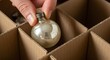 © photoplotnikov - Hand placing vintage christmas ornament into cardboard storage box