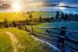 © Pellinni - beautiful rural landscape in mountains on spring equinox. day and night time change concept. road near fence through the pasture with haystack and coniferous trees with sun and moon at twilight