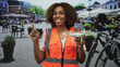 © Krakenimages.com - Woman engineer holding drone points finger up in street cafe wearing reflective safety vest and smiling; technology innovation confidence.