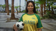 © Krakenimages.com - Woman holding soccer ball on street smiling in green and yellow brasil jersey; pride team spirit community.
