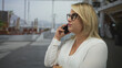 © Krakenimages.com - Woman wearing eyeglasses holds smartphone to ear with folded arms on bustling street in city; concentration.
