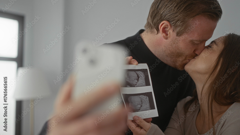 Man and woman joyously taking selfie with ultrasound photo in bright home showcasing pregnancy announcement and new family beginnings.