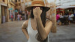 © Krakenimages.com - Woman in straw hat and white tank top raises fist on bustling cobblestone city street near sidewalk cafe tables; defiance.