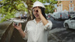 © Krakenimages.com - Woman engineer holding a white quadcopter drone with hand forming ok sign by eye on street in leafy urban setting; innovation confidence.