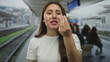 © Krakenimages.com - Young hispanic woman displays hand gesture with lips parted on railway platform at train station; anticipation uncertainty patience optimism.
