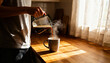 © Hamza - A warm morning moment captured as someone pours steaming coffee into a mug in a cozy kitchen. Sunlight streams through lace curtains, creating delicate patterns on the wooden countertop.