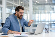 © Liubomir - Angry businessman yelling and pointing at his laptop screen at a modern office desk, showing frustration and stress over a failed project, deadline or technical problem