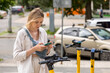 © Nobilior - woman using smartphone while standing near electric scooter on city street